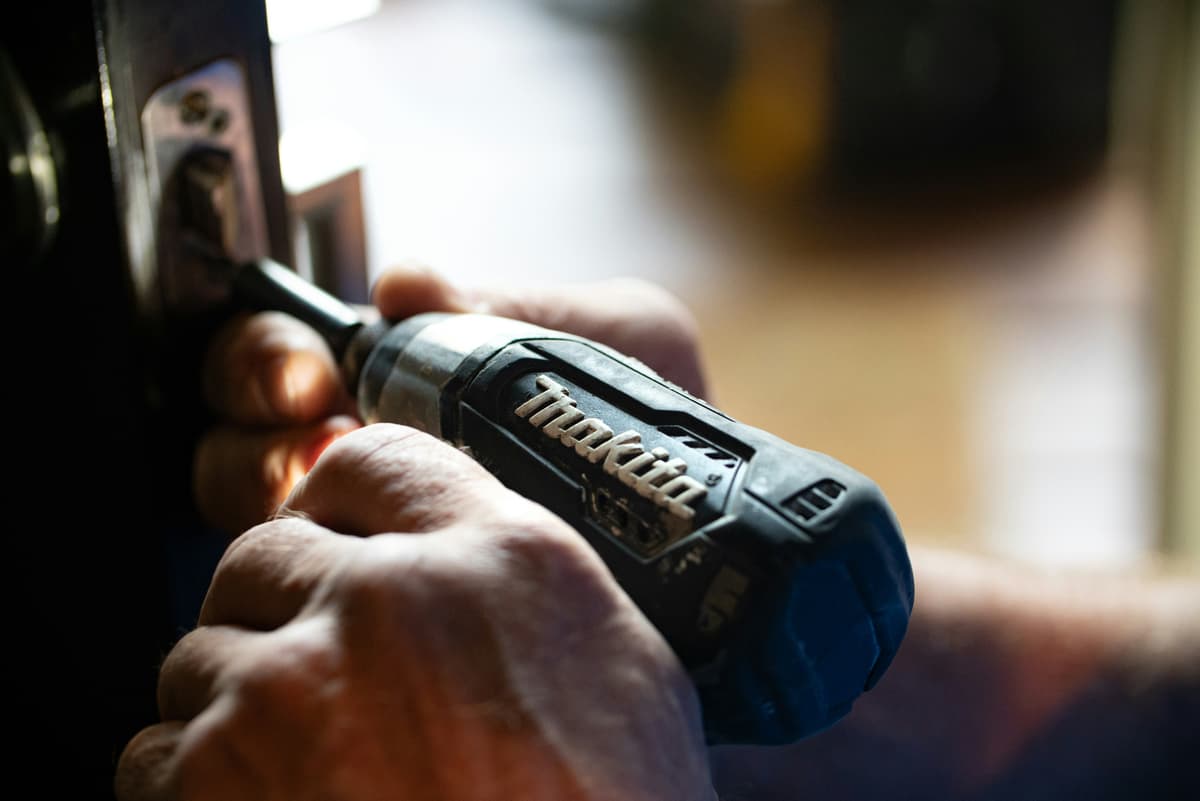 Hands using a Makita drill on a door lock — home maintenance in action